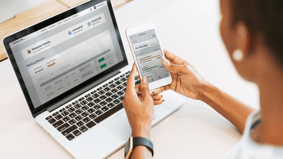 A person holding a phone showing a budgeting app beside a laptop with a financial dashboard of pending requests.