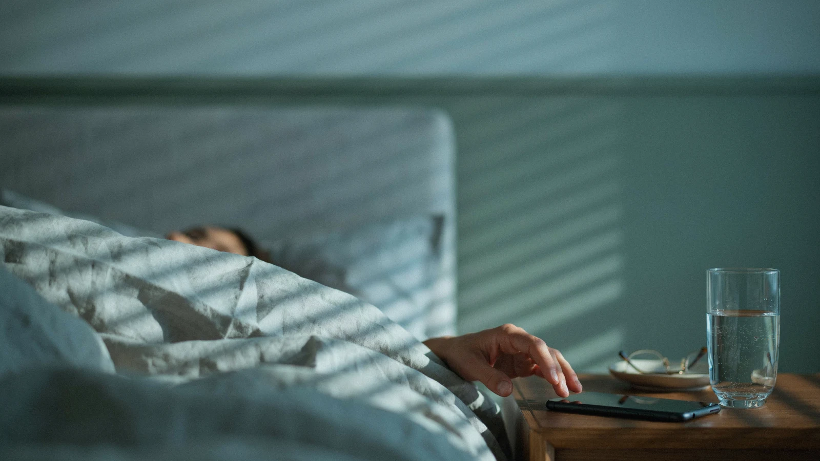 Hand reaching for a phone alarm at dawn, one of the everyday AI examples that decides when you wake