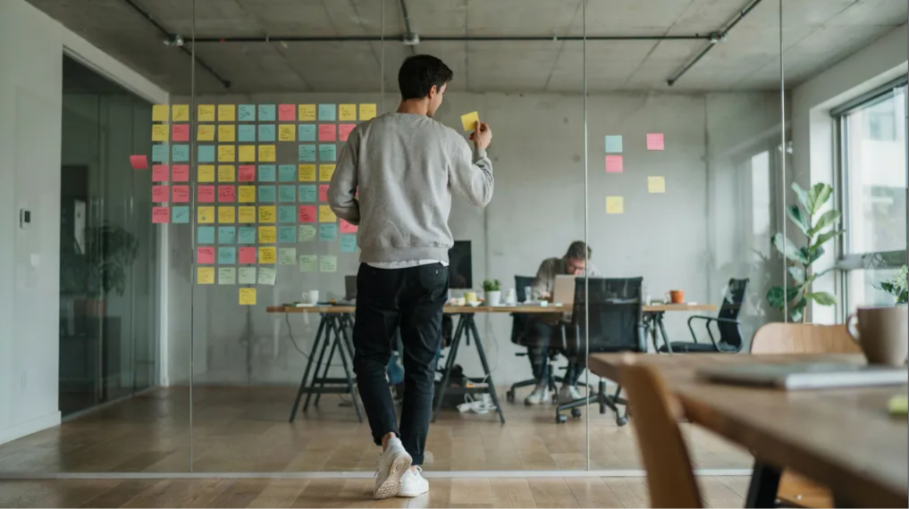 A person arranging sticky notes on a glass wall while planning a software project.