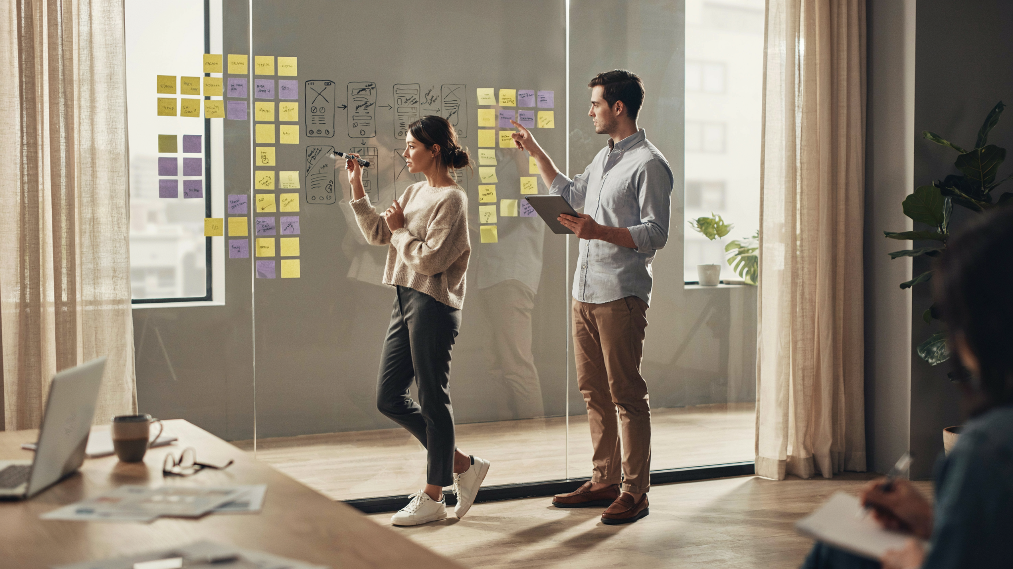 Two people mapping a mobile app's screens with sketches and sticky notes during design and planning.