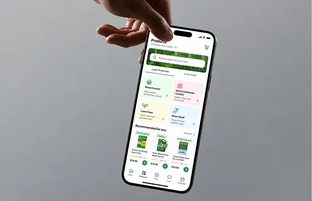 Phone held in a hand showing the products tab: lawn problem and lawn goal tiles above a recommended products row with prices