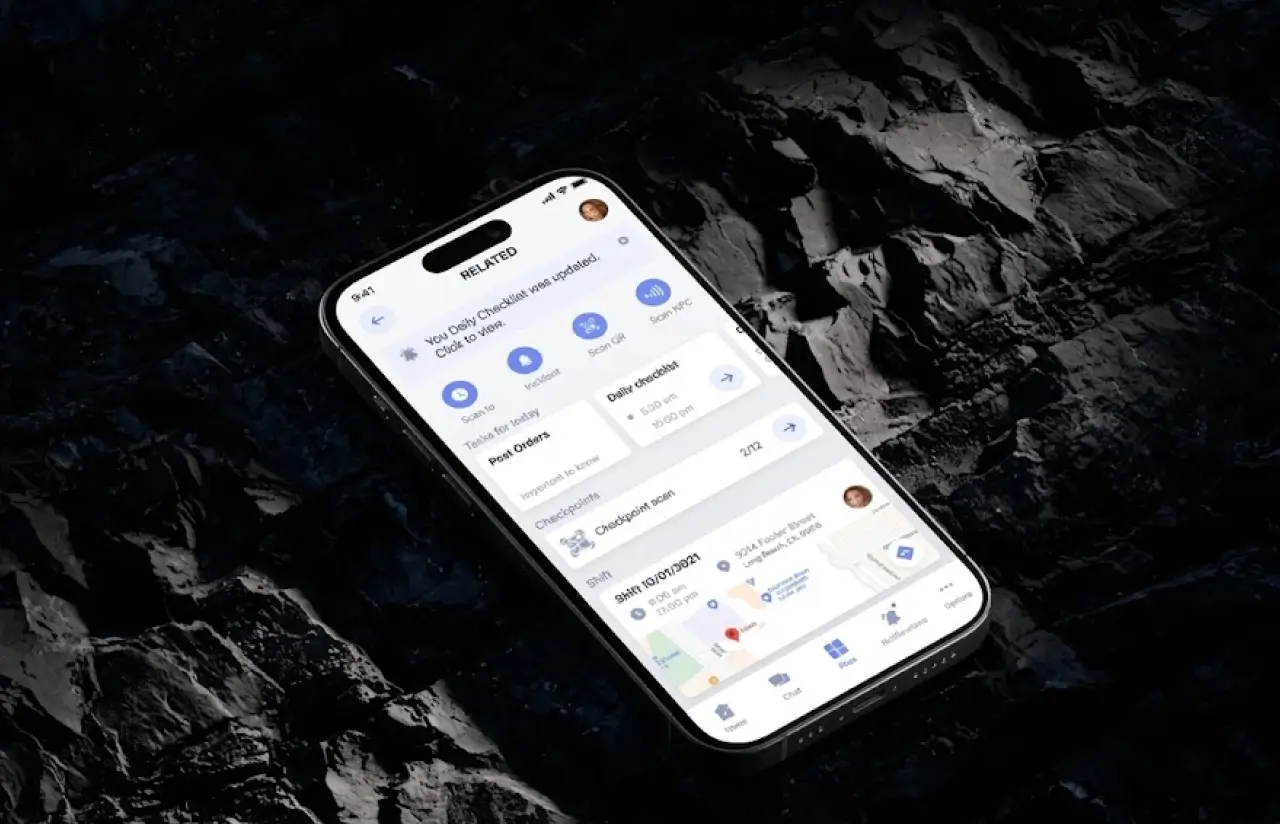 Phone lying on dark rock showing a security guard app home screen with quick actions, tasks for today, checkpoints and the current shift