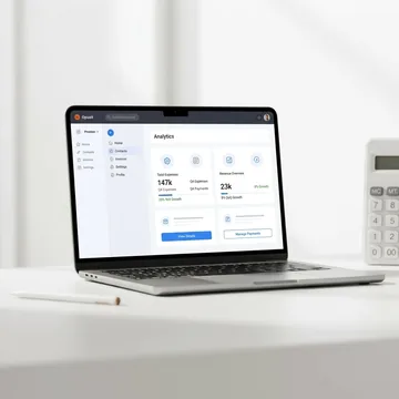 Laptop on a white desk showing a web app analytics dashboard with expenses and revenue, next to a calculator